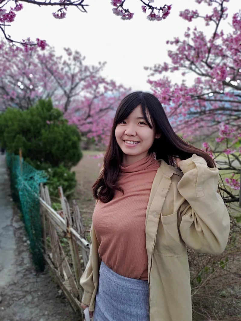 Jeany 站在粉紅色花樹旁微笑