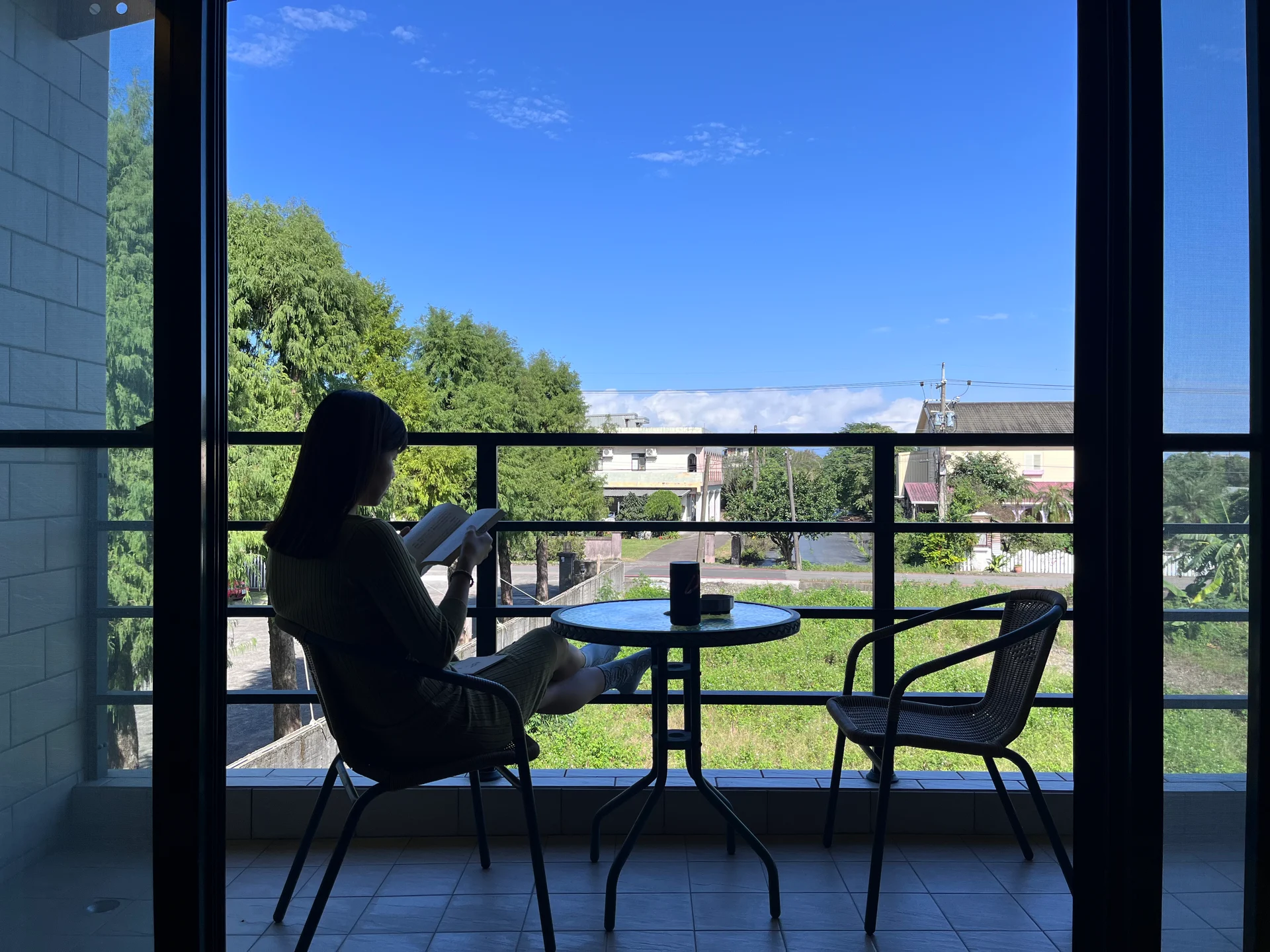 Jeany 坐在窗邊讀書,窗外是藍天、樹木與街景
