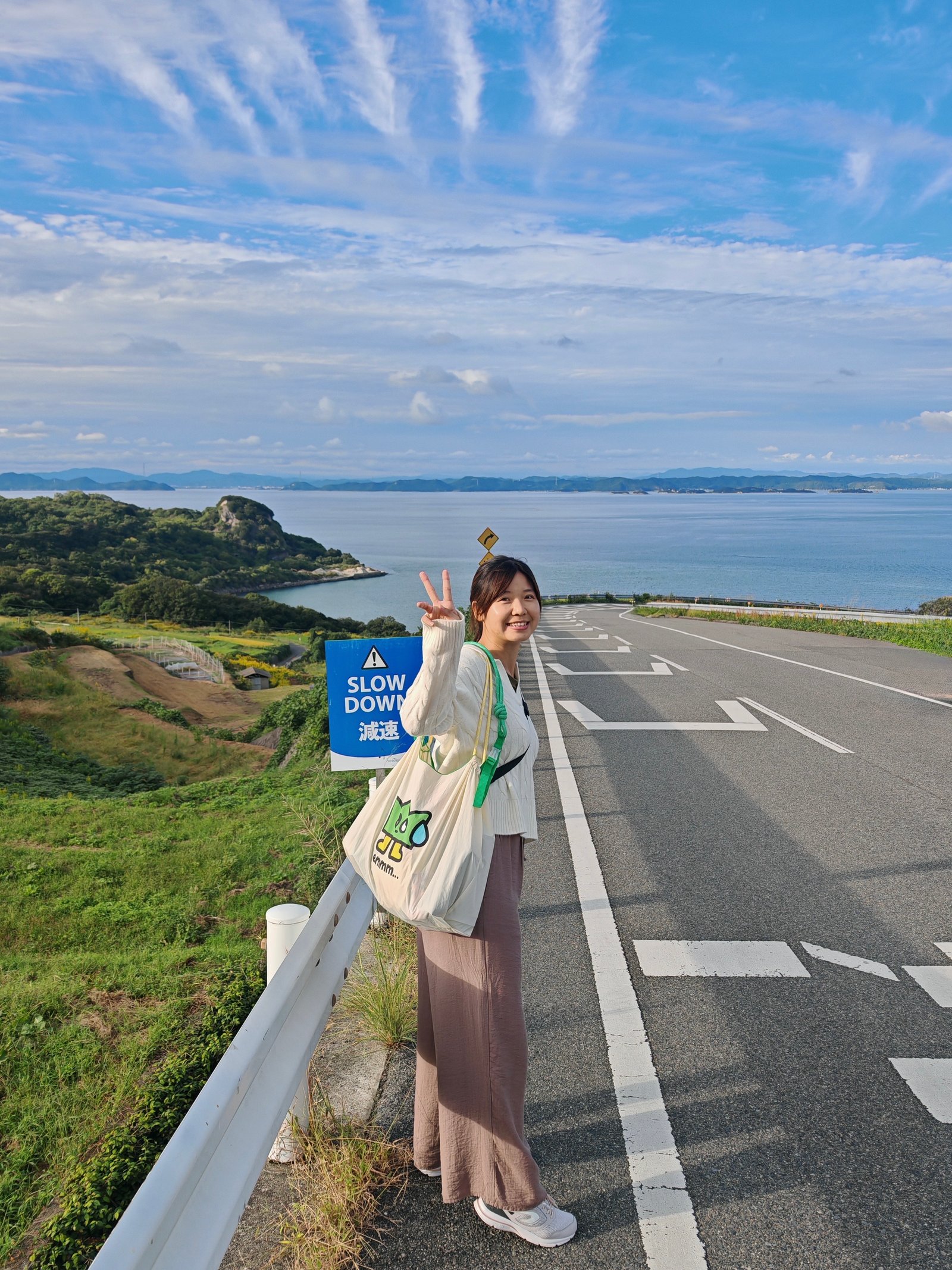 Jeany 漫步在面海的公路旁,路標寫著 SLOW DOWN 減速,藍天與海面一望無際