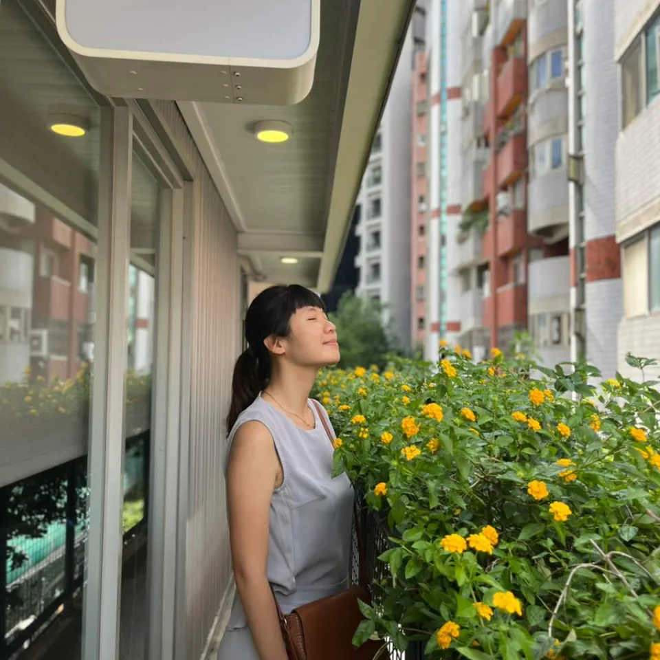 Jeany 站在街邊的黃色花叢旁