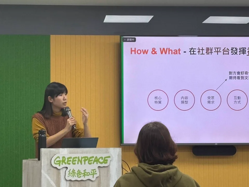 Jeany 手拿麥克風,在投影幕前分享